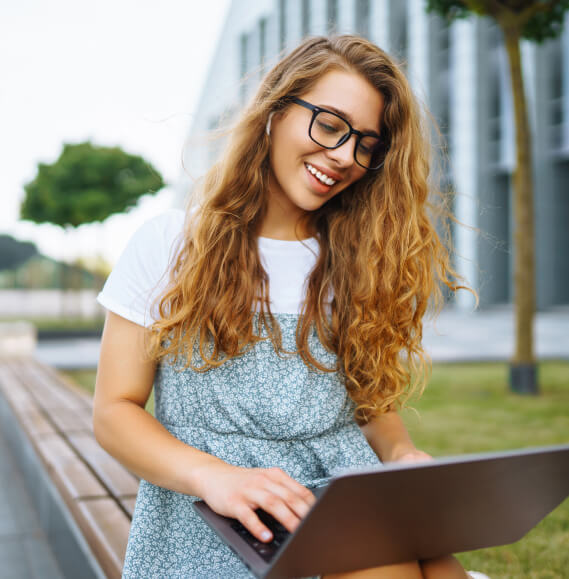 A female student sitting on a bench outside using their laptop