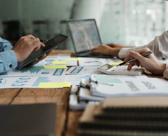 Documents and laptops on a table with people working