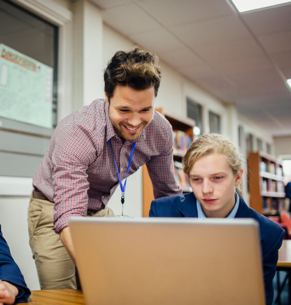 Teacher looking over the shoulder of a student on a laptop