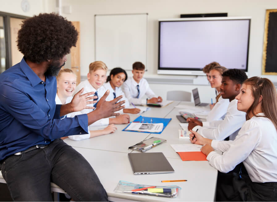 Teacher sitting on the edge of a table speaking to students